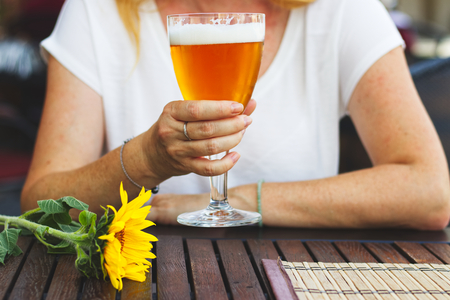 Woman sitting in outdoor restaurant and drinking beer, city life in summer. Woman holding a glass of draft beer in pubの写真素材