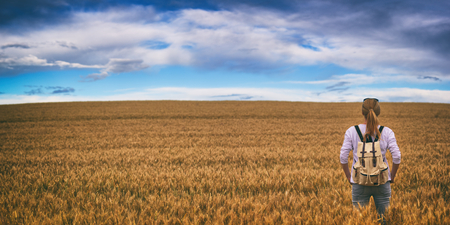 Hiking woman is standing in field and watching horizon with beautiful sky, panorama of countryside, beautiful rural scenery with wheat fieldの写真素材
