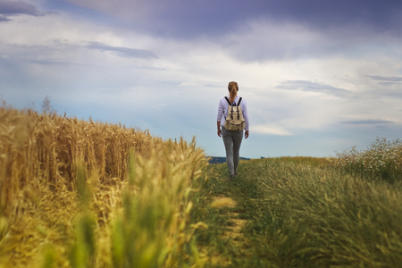 Hiking woman in nature at summer, traveler walking on footpath in the field. Beautiful countryside with dramatic sky. Adventure conceptの写真素材