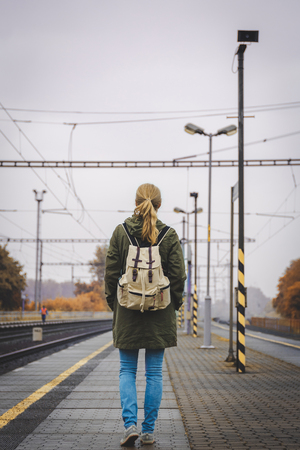Woman with backpack standing at railroad station platform and waiting for a train. Travel concept. Rail transportationの写真素材