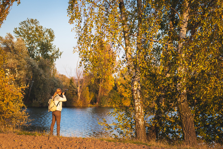 Hiker photographing a landscape at autumn. Woman standing at riverside and taking picture of nature.の写真素材