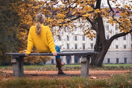 Woman relaxing on park bench at autumn season and looking to castle, Kromeriz, Czech Republic. Blond hair woman sitting on a bench.の写真素材
