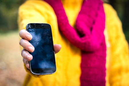 Woman holding a broken smartphone in her hand. Upset woman with damaged mobile phone.の写真素材