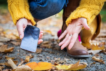 Upset woman and broken smartphone. Woman picking damaged mobile phone from the ground.の写真素材