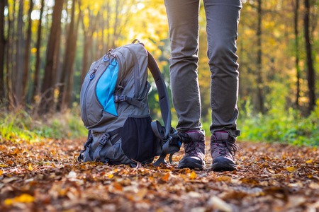 Woman is wearing hiking boot and standing next to backpack in forest at autumn. Travelling in woodland. Hiking concept.の写真素材