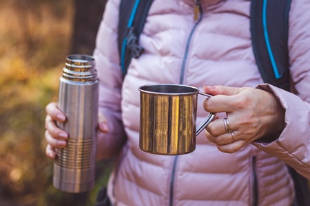 Traveler holding a cup of tea and thermos in forest. Refreshment during hiking.の写真素材