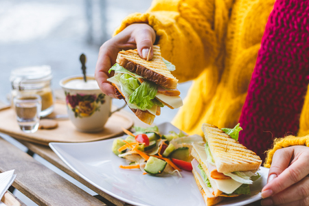 Woman having breakfast in outdoors cafe at city street. Sandwich and coffee on table.の写真素材