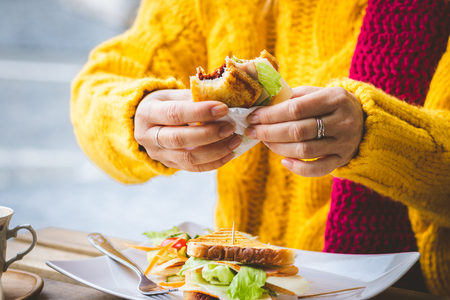 Woman having breakfast in outdoors cafe at city street. Sandwich and coffee on table.の写真素材