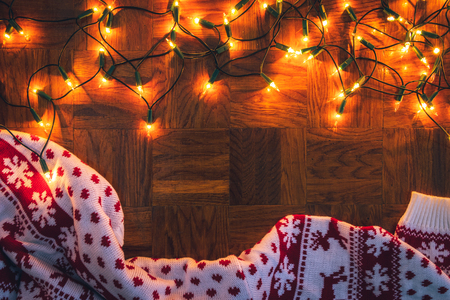 Christmas lights and knitted sweater on wooden background. Merry christmas greeting card. Flat layの写真素材