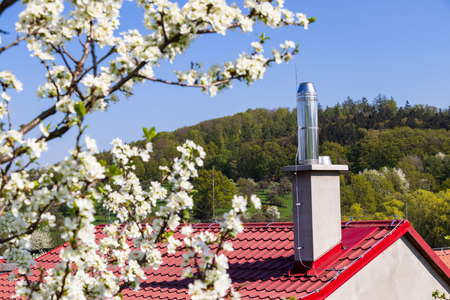 Stainless steel chimney on the house and blooming tree in spring. Modern architecture in private building. Red roof.の写真素材