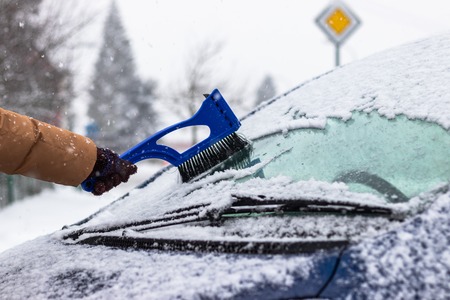 Cleaning car windshield from snow by ice scraper with brush at winter. Remowing snow from car on the street.の写真素材