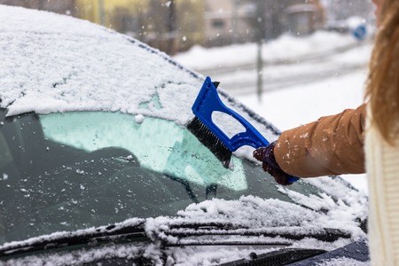 Cleaning car windshield from snow by ice scraper with brush at winter. Remowing snow from car on the street.の写真素材