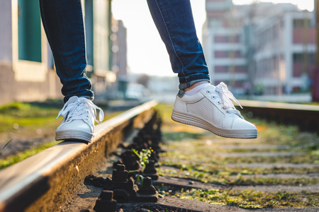 Woman in white sneakers standing on rail track. Walking with sports shoe in cityの写真素材