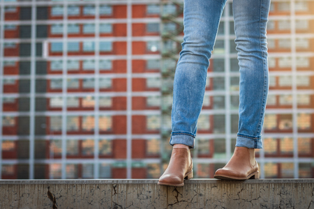 Female legs in jeans and leather shoe. Stylish woman standing in city. Modern architecture backgroundの写真素材
