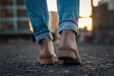 Woman wearing jeans and leather shoe walking in city during sunset. Close-up rear view to shoesの写真素材