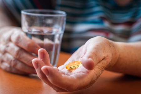 Omega-3 pill and glass of water in senior female hands. Old woman taking fish oil capsule. Medical and healthcare concept with peopleの写真素材