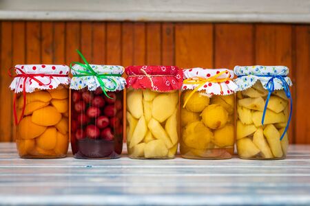 Preserved food in jar, fruit compote on wooden table. Variety of homemade preserved fruit in kitchen. Apricot, cherry, pear, plum and apple compotesの写真素材