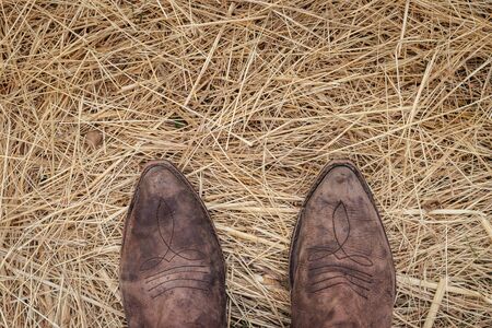 Standing in cowboy boots on golden hay. Old worn out leather boot. Directly aboveの写真素材