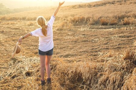 Blond hair woman with arms outstretched enjoying summer in field. Happy carefree woman in rural scene. Concept of happinessの写真素材