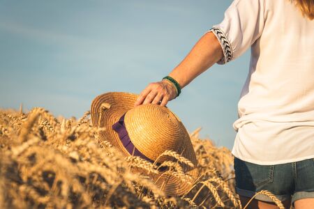 Enjoyment of summer. Woman holding straw hat in her hand and walking in field. Carefree peopleの写真素材