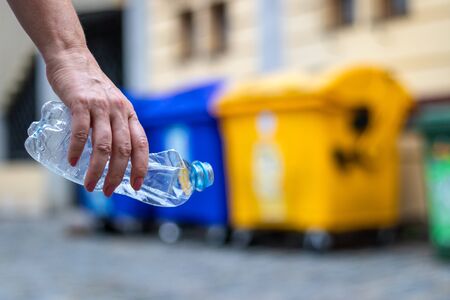 Recycling plastic waste. Hand holding plastic bottle. Garbage bin at city street. Environmental conceptの写真素材