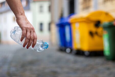 Evironmental issues. Hand holding plastic bottle at city street. Recycling plastic wasteの写真素材