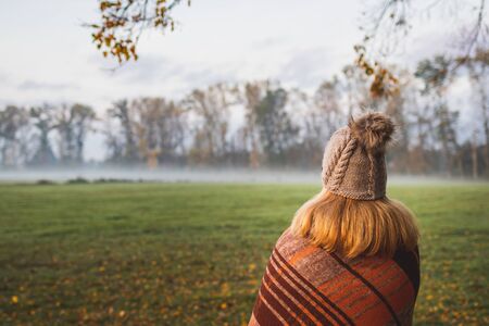 Woman with blanket and knit hat enjoying cold misty morning outdoors. Enjoyment of nature. Female wearing warm clothingの写真素材