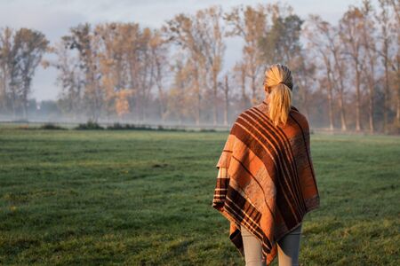 Woman with woolen blanket enjoying tranquil scene at foggy morning at nature. Mist over countryside. Female covered by warm blanket outdoorsの写真素材