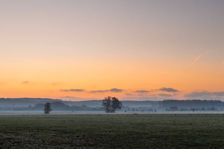Sunrise over fog at countryside. Tranquil scene at misty morning over pasture. Colorful dawn at countrysideの写真素材