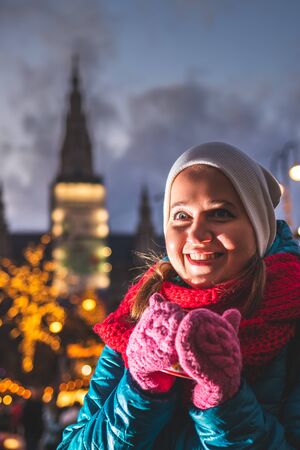 Young woman drinking mulled wine at christmas market in Vienna, Austria. Happy tourist enjoying vacation during christmas holiday. Hot drink in female hands with knitted gloveの写真素材
