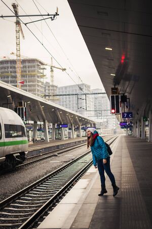 Young woman tourist waiting for train at railroad station. Female backpacker looking to arriving...