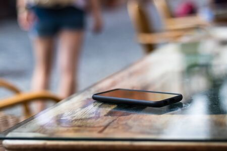 Woman leaving from street restaurant where she forget her mobile phone. Lost smart phone on table at outdoor cafe. Selective focusの写真素材
