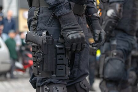 Close-up view to armed police officer with gun. Special force with armored uniform standing at city streetの写真素材