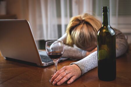 Drunk woman with open laptop sleeping on table after drinking alcohol. Red wine glass in female...