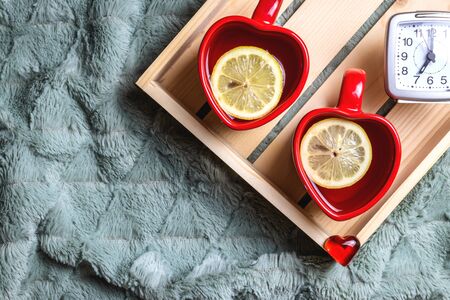 Serving lemon tea on tray at morning on valentines day. Romantic wake up. Hot drink in heart shape tea cup and alarm clock. Home sweet homeの写真素材