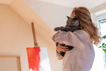 Woman holding her cute cat in art studio. Female artist trying find the inspiration before painting.の写真素材