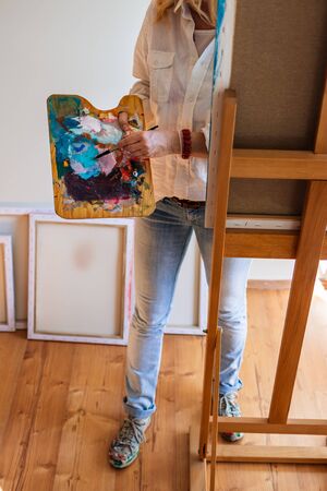 Woman artist mixing acrylic colors at palette and working on paintings. Painter in art studio. の写真素材