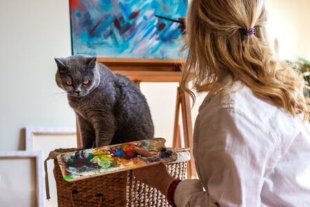 Woman and her pet in art studio. Artist enjoying painting with her british shorthair cat. Craft and leisure activity indoorsの写真素材