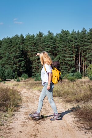 Woman hiker with backpack walking on footpath in nature. Female tourist hiking outdoors during summer day aloneの写真素材