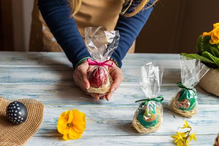 Woman holding wrapped easter eggs as gift for Easter holiday celebration. Making decoration on wooden table at homeの写真素材