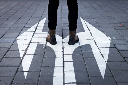 Make decision which way to go. Walking at directional sign on road. Choice concept with human legs and arrow symbol on streetの写真素材
