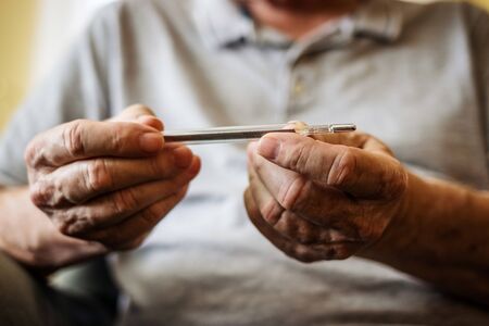 Senior man is measuring his body temperature by thermometer. Coronavirus, flu virus and fever. Healthcare concept with peopleの写真素材