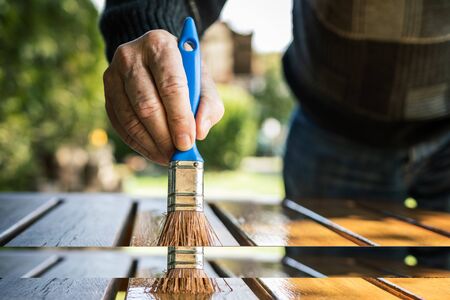 Craftsman painting wooden table. Senior man restoring of garden furniture. Close up hand with paintbrush. Renovation by paint of wood plankの写真素材