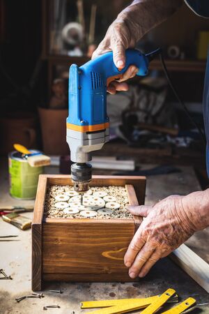Carpenter making wooden insect house or hotel. Craftsperson using drill in workshop. Carpentry workの写真素材