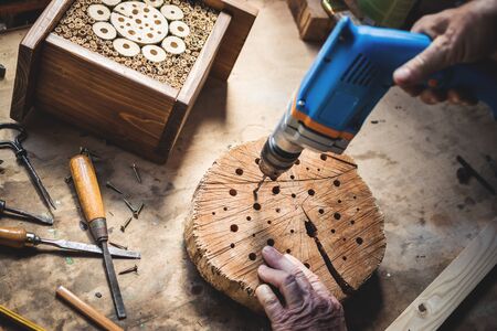 Craftsperson making wooden insect house. Carpenter using drill in workshop. Manual worker doing decorative insect hotelの写真素材