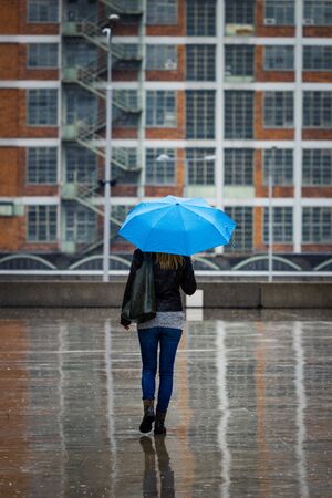 Woman with umbrella walking in city at rain. Trendy woman wearing street style casual clothing. City life during bad weatherの写真素材