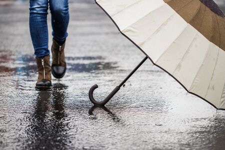 Umbrella at street in rain. Walking legs in puddle in background. Rainy day and bad weather at cityの写真素材