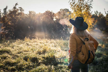 Woman with hat and backpack enjoying cold autumn morning during hiking outdoors. Tourist in natureの写真素材