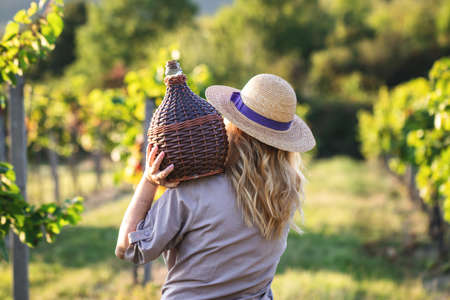 Woman with demijohn at vineyard. Tradition harvest festival. Young woman holding carboy with wineの写真素材