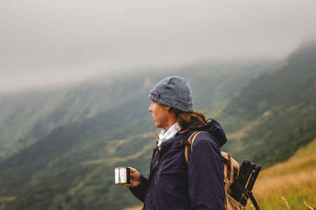 Hiker holding cup with hot drink in mountain at bad weather. Travel, adventure and active lifestyle conceptの写真素材